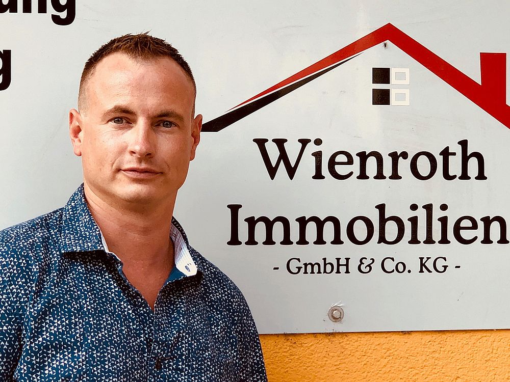 Thomas Wienroth vor Immobilienmakler-Logo